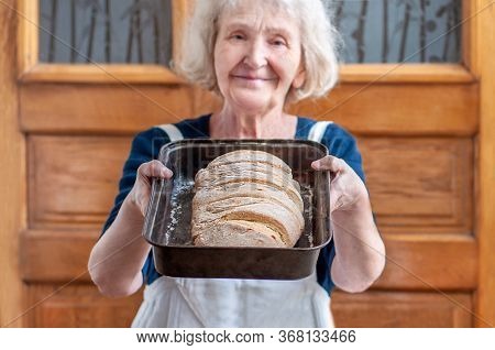 Elderly Grandmother Bakes Bread At Home On Quarantine Covid-19. A Good Housewife With Homemade Bread