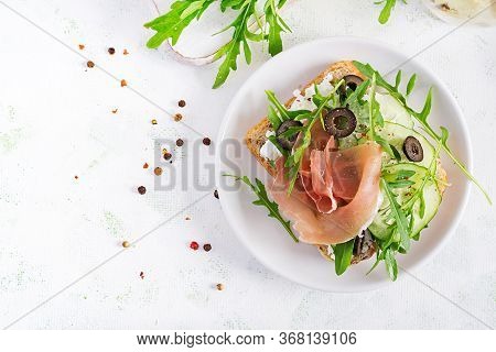 Sandwich With Prosciutto, Cucumber, Black Olives, Arugula And Feta Cheese On  Table.  Trend Food. To