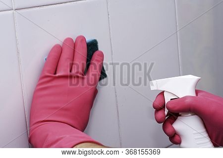 Bman In Rubber Household Gloves With A Sponge And Spray Washes A White Tiled Wall
