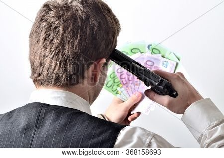 Pistol At The Head - A Man Committing Suicide By Handgun - Holding Euro Banknotes In Hand At Backgro
