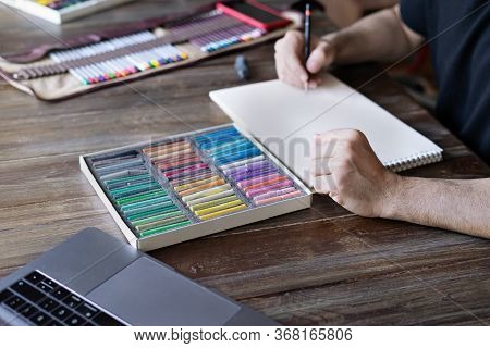 Man Artist Painting With Pencil And Pastel Crayon Chalks On Paper In Front Of Laptop. Learning Paint