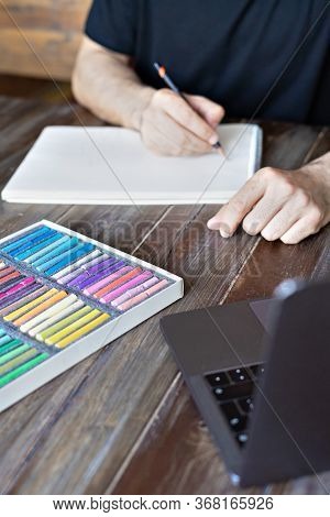 Man Artist Painting With Pencil And Pastel Crayon On Paper In Front Of Laptop. Learning Painting Onl