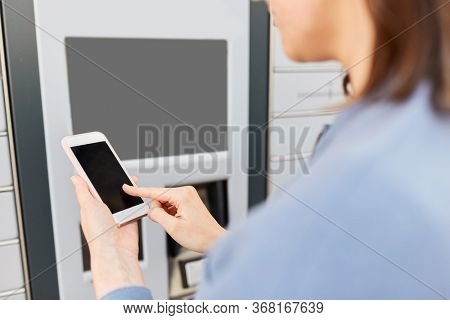 mail delivery and post service concept - close up of woman with smartphone choosing operation on outdoor automated parcel machine's touch screen