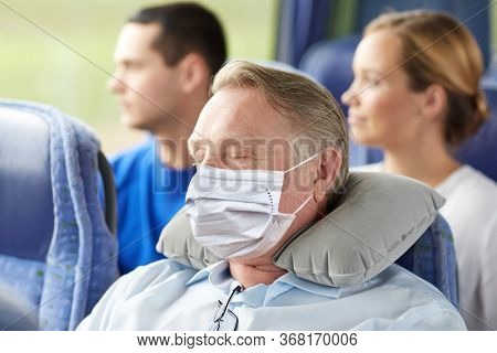 tourism, healthcare and pandemic concept - senior man wearing face protective medical mask for protection from virus disease sleeping in travel bus with neck pillow