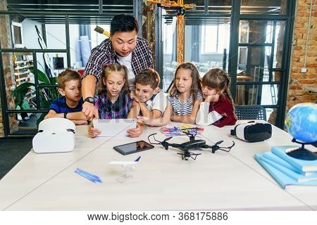 School Teacher At Desk Works With Five Young Pupils Using Digital Tablet Computer In Technology Clas