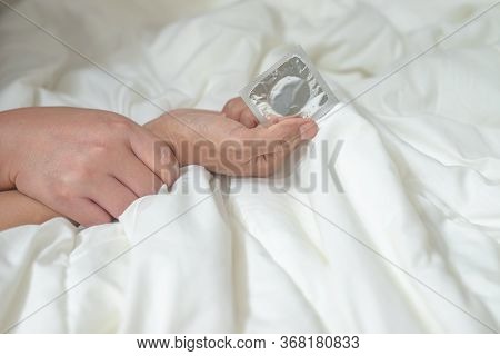 The Hands Of The Man And Woman Are Touching On The Bed With The Woman's Hand Holding A Condom Ready 