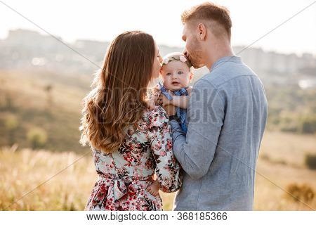 Mom, Dad Kissing Their Little Girl On Summer Day. Mothers, Fathers And Babys Day. Happy Family For A