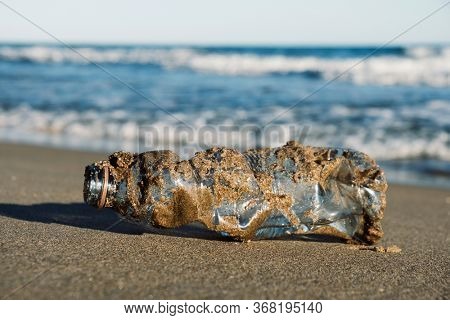 closeup of a used plastic bottle, covered with wet sand, on the sand of a lonely beach, brought back by the ocean to the seashore