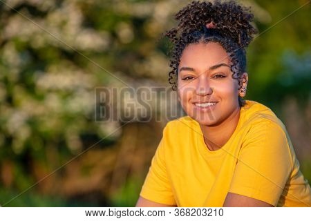 Beautiful biracial mixed race African American teenager teen girl young woman smiling with perfect teeth outside at sunset or sunrise