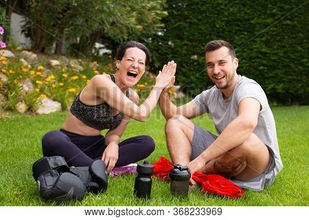 Joyful Couple Of Fighters Enjoying Break During Outdoor Workout, Sitting On Grass, Giving High Five.
