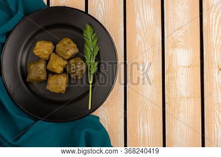 A Top View Dolma Green Dolma With Minced Meat Inside Black Plate On The Brown Wooden Desk