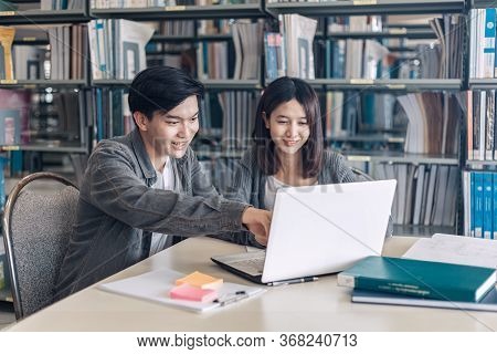 High School Or College Students Studying And Reading Together In Library. Student Use Laptop At Libr