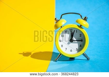 Yellow Vintage Alarm Clock On A Blue And Yellow Background With Selective Focus, Copy Space For Text