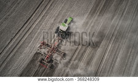 Aerial View Of A Clean Field In Which The Tractor Makes Vertical Tillage. Red Tillage Equipment And 