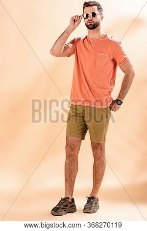Stylish Young Man Posing In Shorts, Summer T-shirt And Sunglasses On Beige