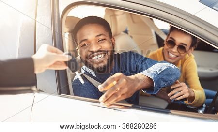 Car Sales. Cheerful Black Couple Taking Key From Automobile Dealer For Test Drive Sitting In Auto. P