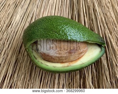 Two Halves Of Avocado With Bone On A Straw. Green, Ripe Avocado Vegetable In A Cut. Halves Persea Ex