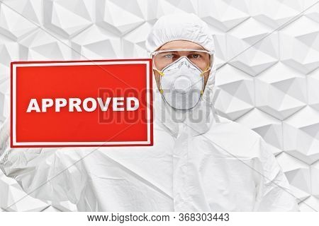 COVID-19 concept. A doctor in a protective suit holds a sign approved on a white background. Copy space.