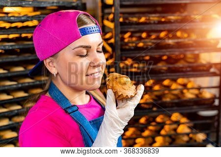 Young Happy Female Worker In Sterile Cloths Holding Freshly Baked Muffins On Tinplate Inside Food Pr