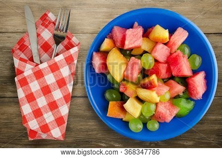 Fruit Salad On A Brown Wooden Background. Vegetarian Salad Of Fruit On A Blue Plate With Fork Ank Kn