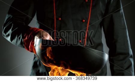 Closeup of chef holding empty wok pan in fire, ready to prepare for cooking.