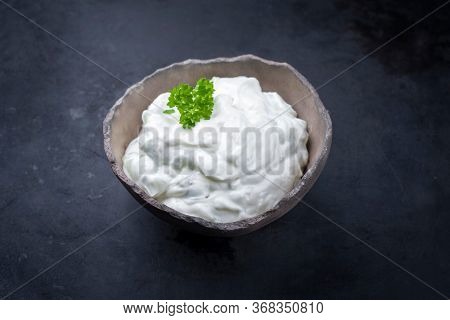 Traditional Greek tzatziki fat yogurt offered with parsley as closeup in a rustic modern design bowl with copy space 