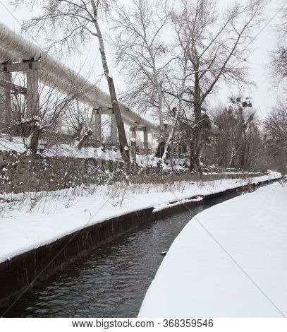 Urban Stream In Winter. The Lybid River (kyiv, Ukraine) In The Snow. Elevated Pipeline Near The Rive