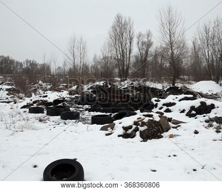 Old Used Tire Covers And Other Garbage In The Snow On The Landfill In Winter. Environmental Pollutio