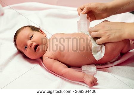 Mother Putting On Diaper On Two Weeks Old Child. Infant Baby Girl Lying On Back With Open Mouth Whil