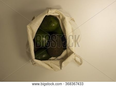 Different Varieties Of Avocado Ripen In A Light Canvas Bag On A White Background. Top View