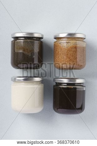Vegan Organic Paste Of Flax Seeds, Milk Thistle, Peanuts And Coconut In Glass Jars On Light Blue Bac