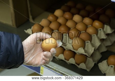 Close-up Of A Hand In A Protective Rubber Glove Holding A Medium-sized Brown Egg, Against A Backgrou