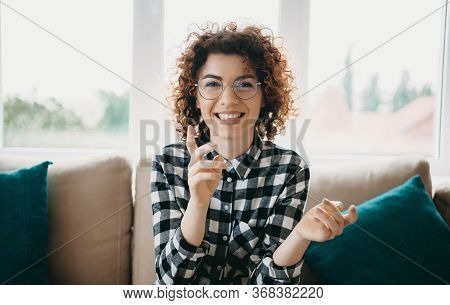 Cheerful Caucasian Woman With Curly Hair And Eyeglasses Smiling At Camera While Sitting Near The Win