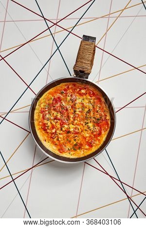 Omelette with tomatoes and seasoning. Beaten eggs with sauce served in iron frying pan. Culinary art. Freshly made dish garnished with herbs top view. Delicious healthy breakfast. Tasty meal