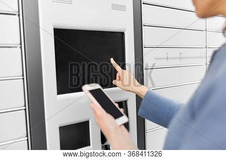 mail delivery and post service concept - close up of woman with smartphone choosing operation on outdoor automated parcel machine's touch screen