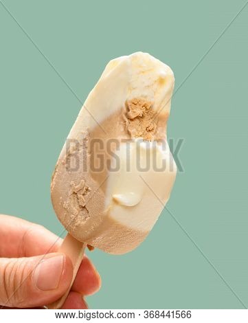 Hand Holding A Cheese And Lemon Flavor Popsicle With A Bite On Green Background