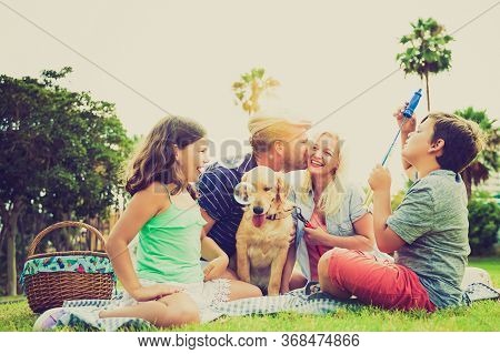 Mother, Father, Sons And Their Dog In A Happy Summer Time Laughing, The Boy Playing With Soap Bubble