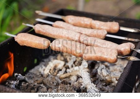 Close Up Of Toasted Sausages On Skewers. Succulent Kupaty Roasting On Chargrill. Concept Of Picnic O