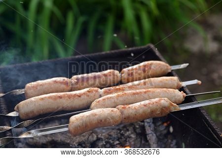 Close Up Of Toasted Sausages On Skewers. Succulent Kupaty Roasting On Chargrill. Concept Of Picnic O