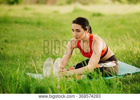 Young Woman Practising Yoga In The Open Air In The Nature On The Grass On The Sunny Day. Outdoor Spo