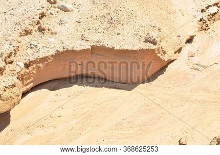 Background Of Yellow Sand With Small Stones After Rain. Soil Erosion After Heavy Rainfall And Precip