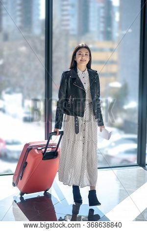 Brunette Female In Leather Jacker Walking With Red Suitcase, Smiling