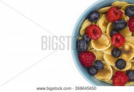 Close Up Top View Mini Tiny Pancake Cereal With Berries In A Blue Bowl On Ehite Background. Breakfas