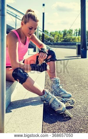 Young attractive woman adjusting safety gear while wearing rollerblades