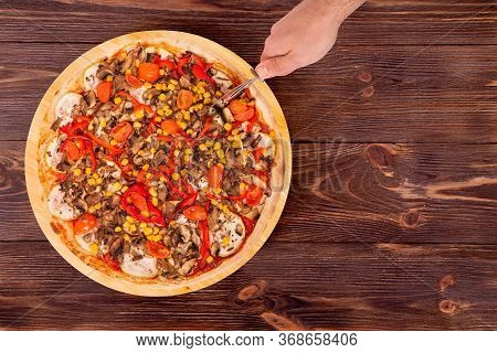 Man Cut The Pizza With A Pizza Cutter, Top View And Copy Space. Delicious Pizza With Mushrooms, Corn