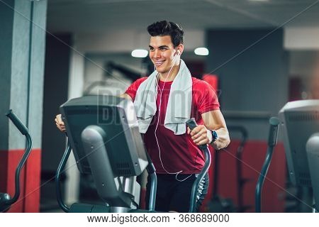 Young Man Doing Exercise On Elliptical Cross Trainer In Sport Fitness Gym Club