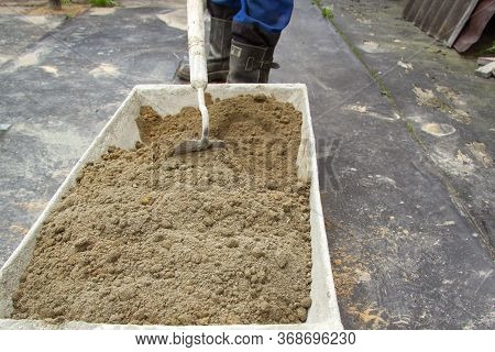 The Man Stirs Sand And Cement In A Large Trough To Make The Solution.