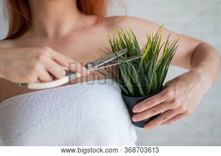 Faceless Red-haired Caucasian Woman Wrapped In A White Terry Towel Shears A Potted Plant With Scisso