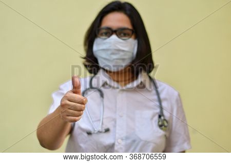 Portrait Of A Young Medical Healthcare Female Worker Showing Thumbs Up Sign With Her Right Hand Wear