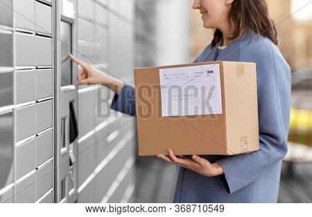 mail delivery and post service concept - close up of happy smiling woman with box at outdoor automated parcel machine choosing operation on touch screen